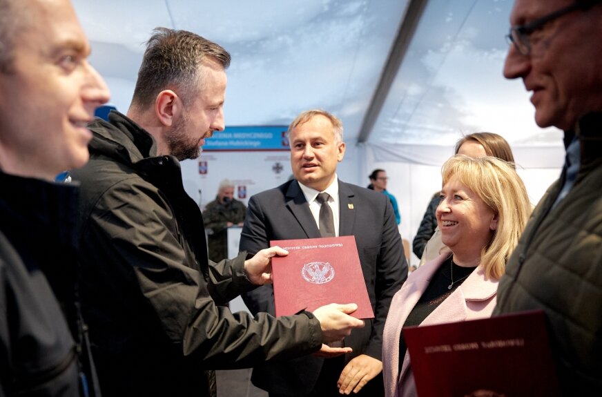 Wojewódzki Szpital Zespolony im. Stanisława Rybickiego w Skierniewicach przystąpił do programu „Szpitale Przyjazne Wojsku” MON. Program ma zacieśnić współpracę cywilno-wojskową w ochronie zdrowia: formalizuje kanały koordynacji z Dowództwem Wojsk Medycznych, zapewnia dostęp do szkoleń z medycyny pola walki, włącza placówki w ćwiczenia ewakuacji medycznej (m.in. COMBAT EVAC SEQUENCE) oraz wspiera inwestycjami infrastrukturalnymi. W regionie łódzkim do szpitali trafić ma blisko 10 mln zł na agregaty prądotwórcze, modernizację piwnic pełniących funkcję schronową, remonty wentylacji i zakup ambulansów.